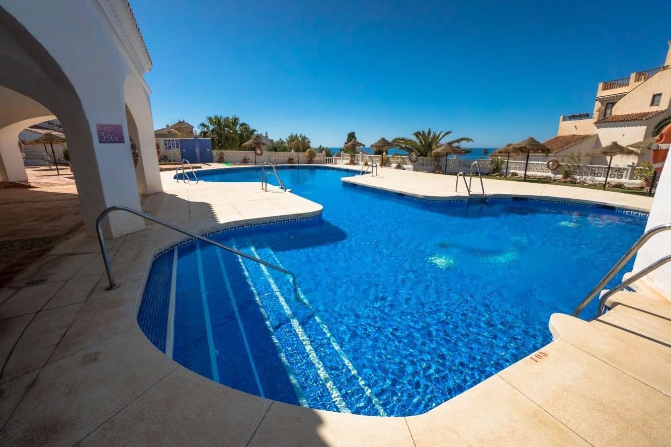 Communal pool with steps and sea view beyond the parasols