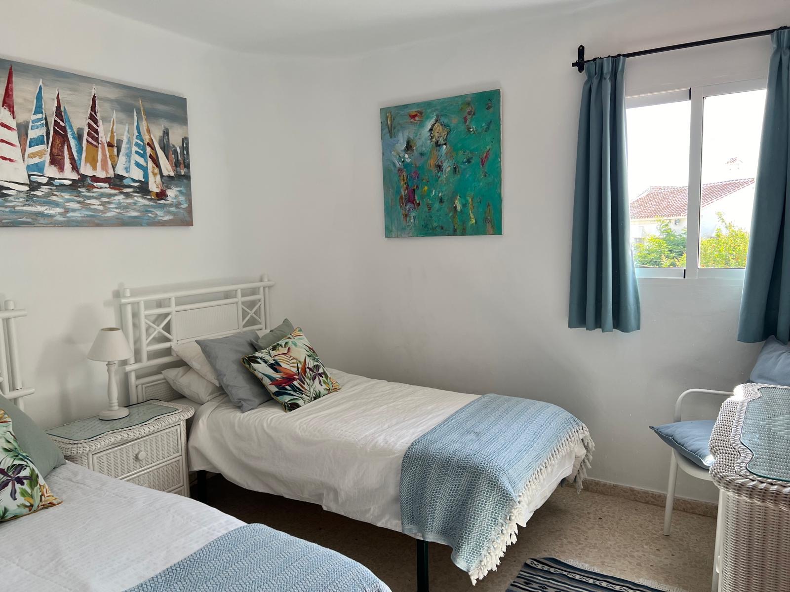 Twin bedroom with white wicker furniture and nautical paintings