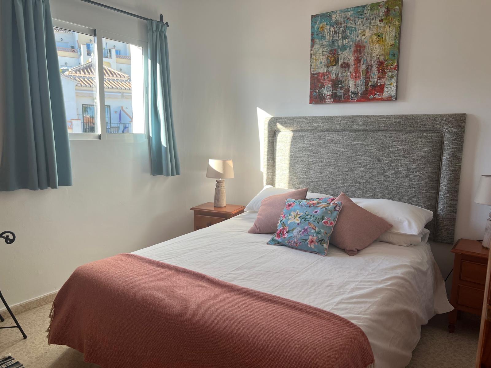 Master bedroom with double bed, grey headboard and colourful artwork